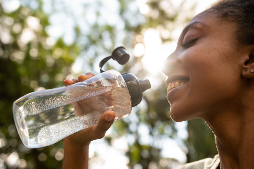 woman who is outside drinking out of bottle with sun shining behind her in Los Angeles