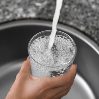 Unrecognizable female hands pouring tap water into a glass from a faucet
