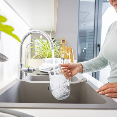 Close up of a woman filling a glass jug with water directly from the tap in the kitchen